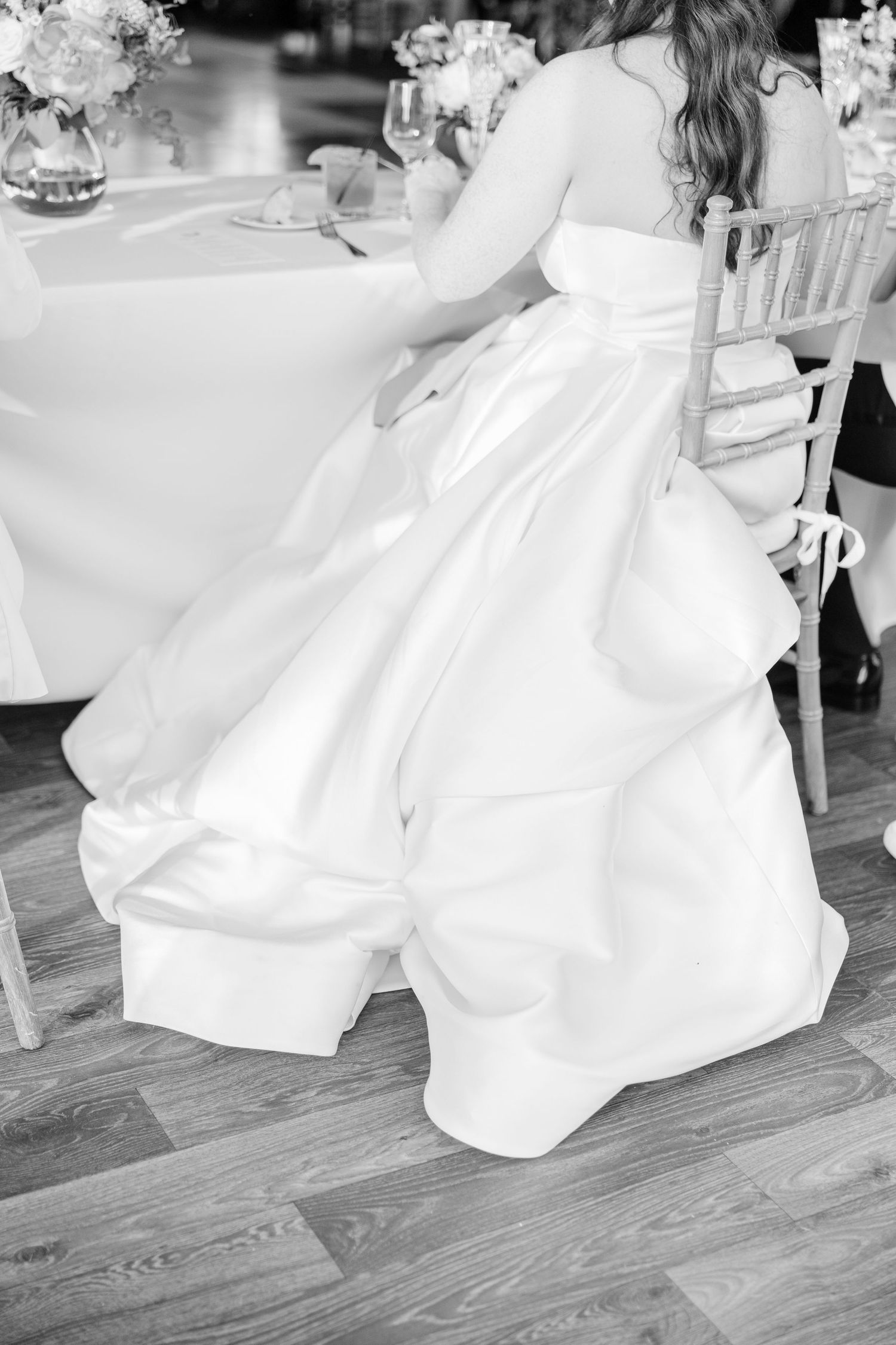 A bride in a flowing white wedding gown twirls gracefully on a hardwood dance floor during her wedding celebration.