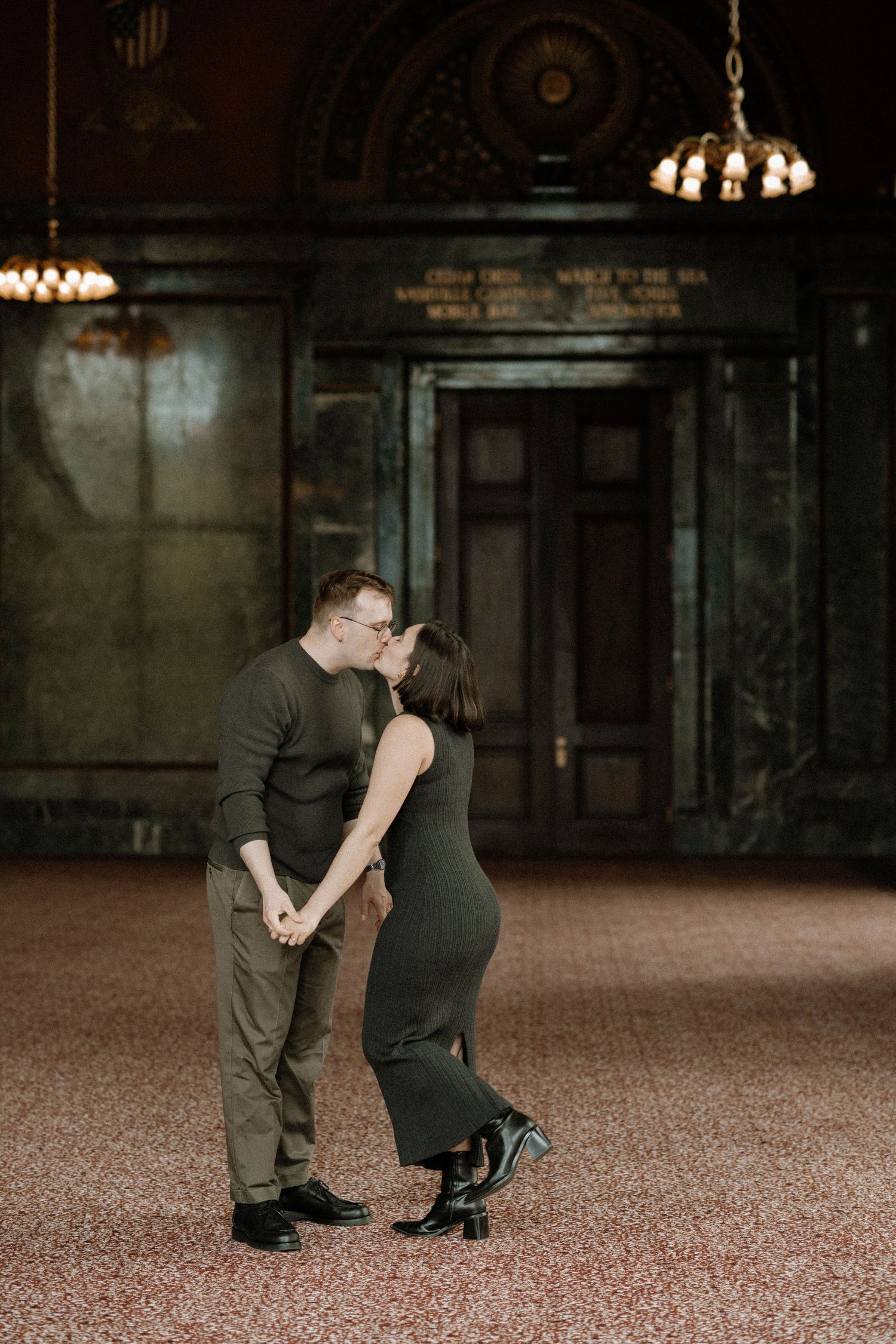 Wedding couple poses together in a formal setting with an American flag and decorative elements in the background.
