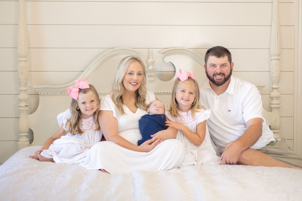 Family lounging together on white bedding in casual attire.