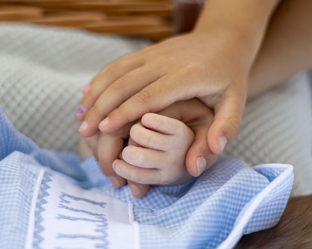 Close up of tiny baby hands grasping a light blue checkered blanket.