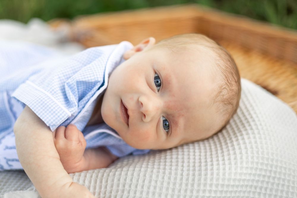 Baby in light blue clothing resting peacefully on white bedding.