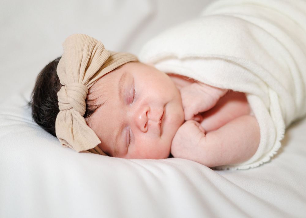 A sleeping baby wrapped in soft white fabric lies peacefully against a light background.