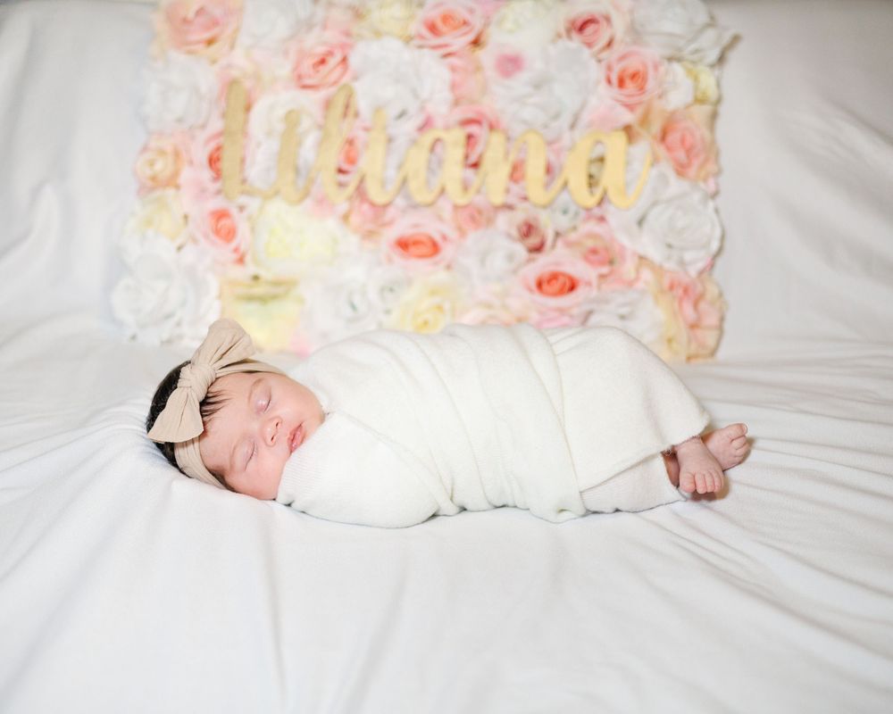 A swaddled newborn sleeping against floral backdrop with text.