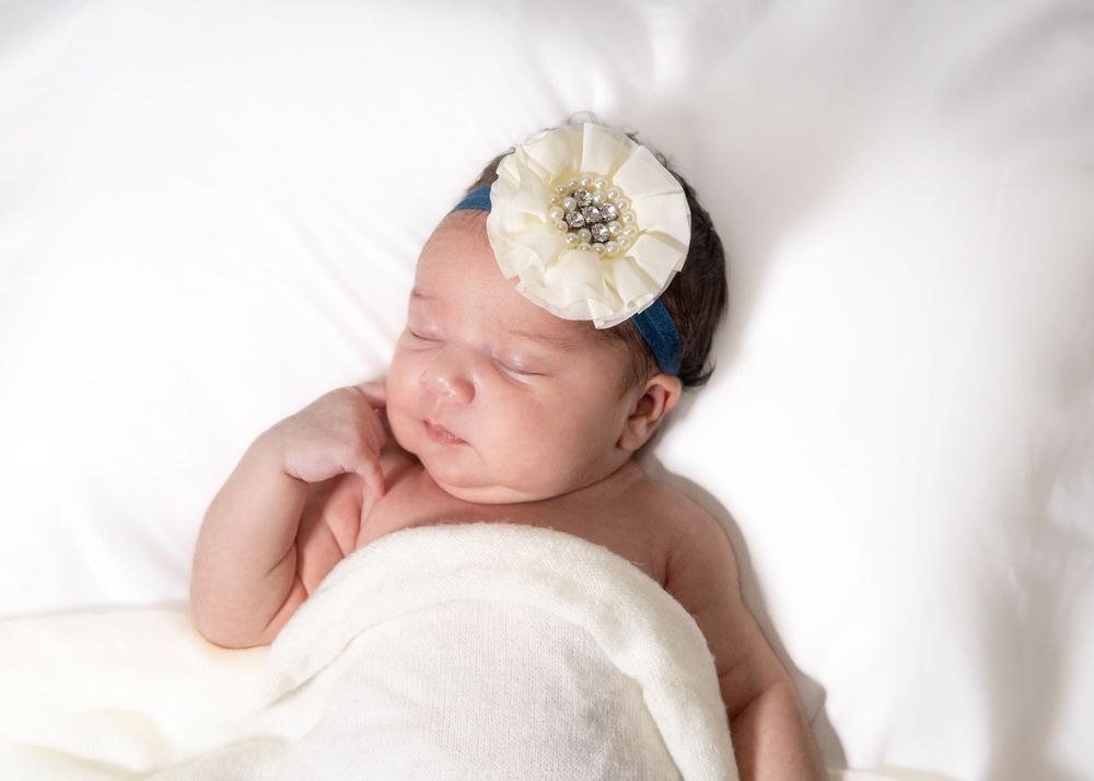 Sleeping newborn baby in white blankets wearing a delicate floral headband.