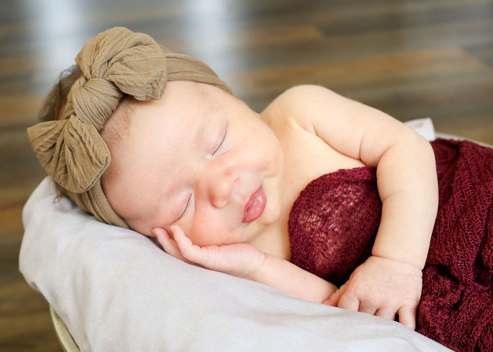Baby sleeping soundly in burgundy outfit on white cushion.
