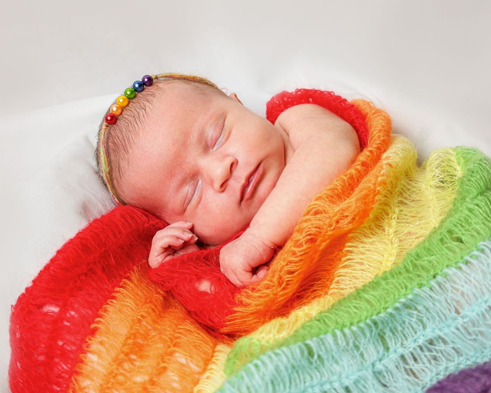 Newborn sleeping on vibrant rainbow colored textured blanket.