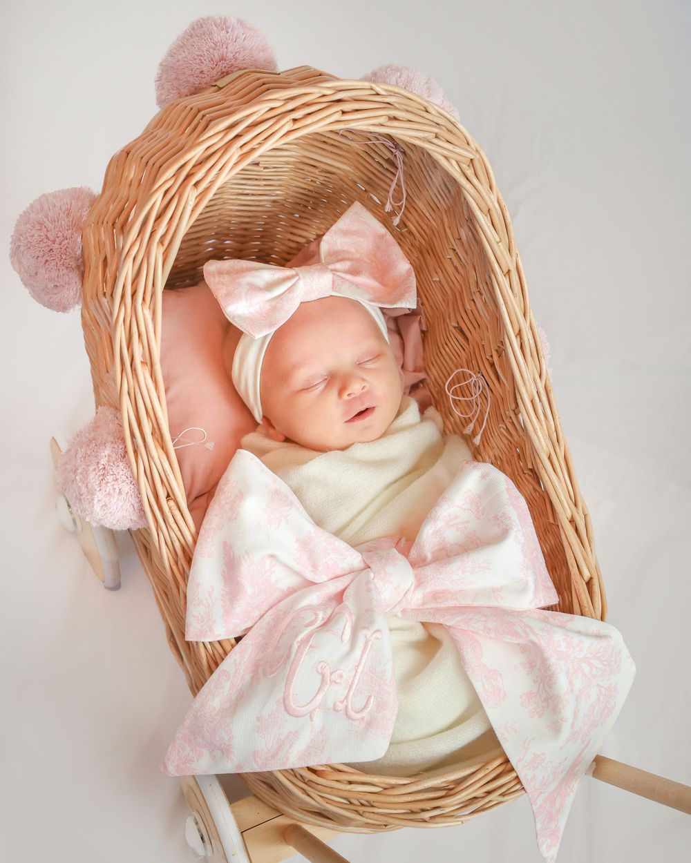 Baby sleeping in wicker basket with pink bow and delicate white blanket.