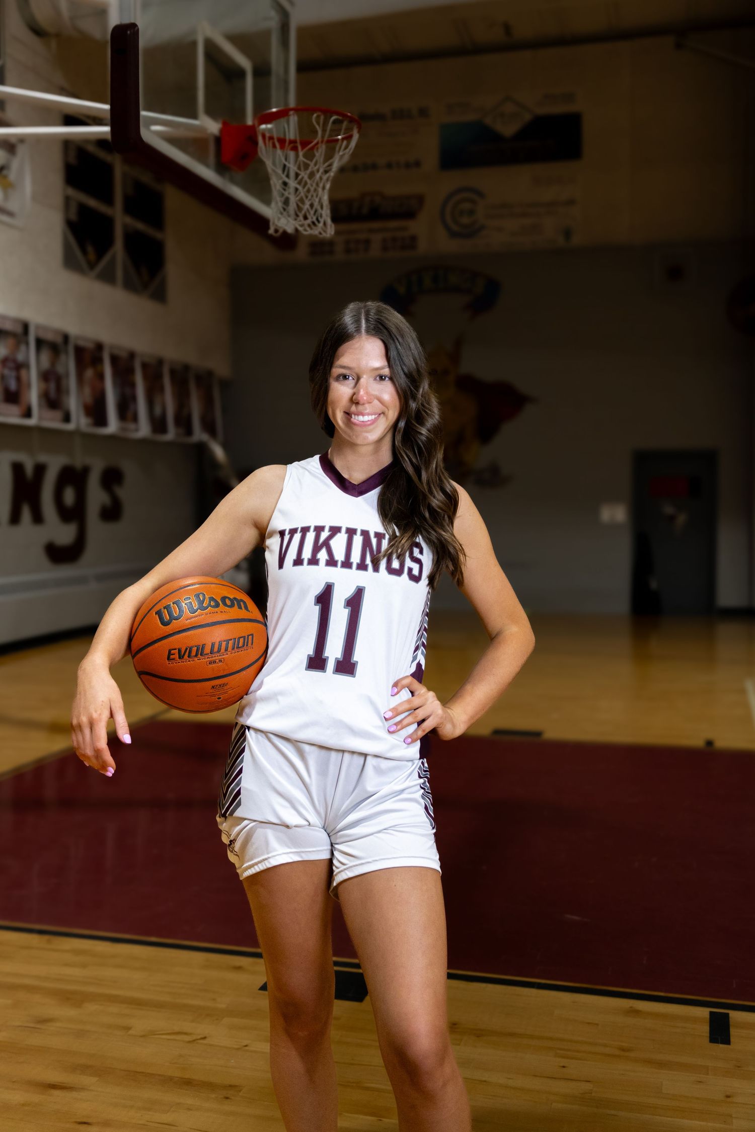 Basketball player in white Vikings jersey poses with ball in gymnasium.