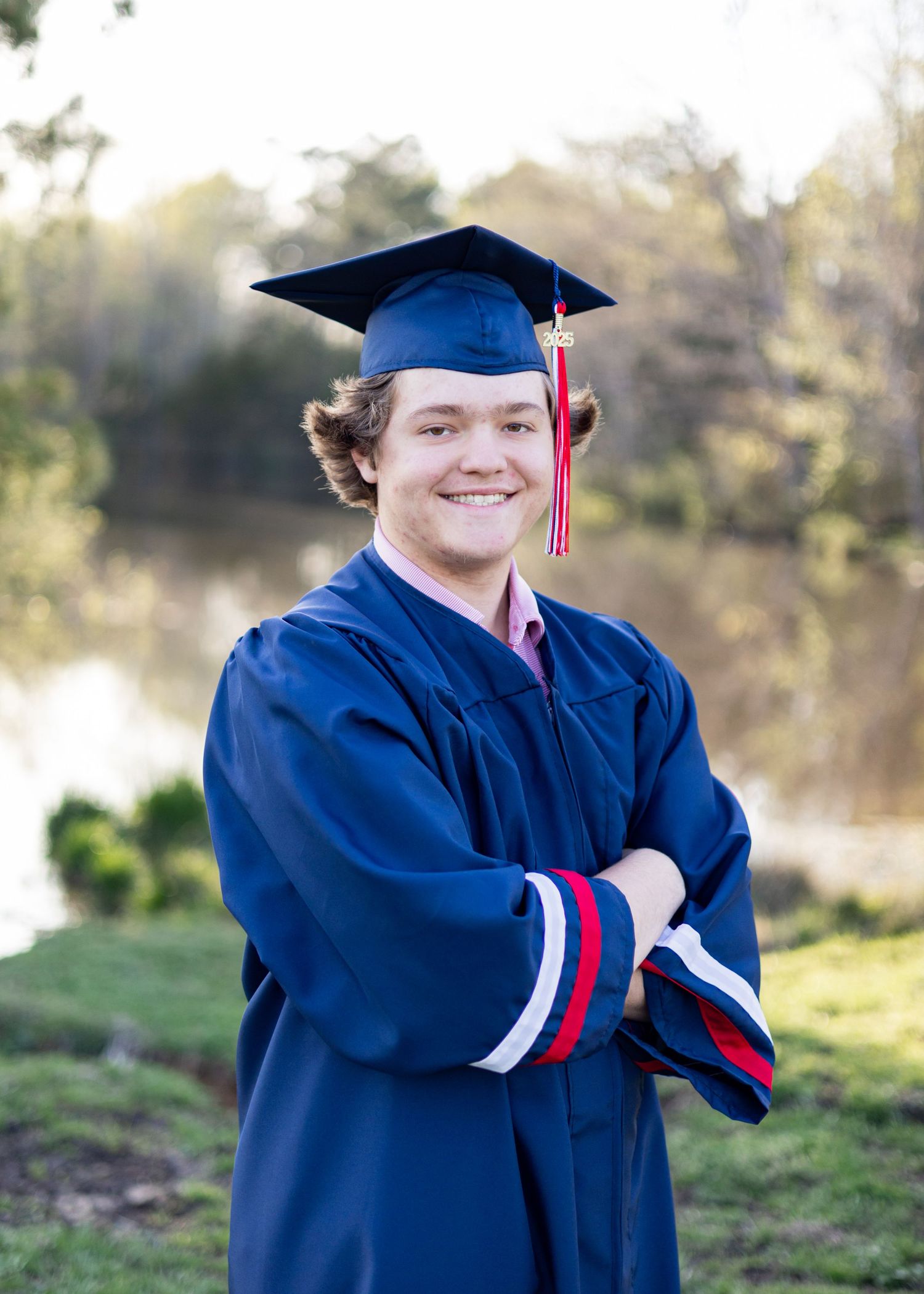 Graduate in blue cap and gown poses outdoors during commencement ceremony.