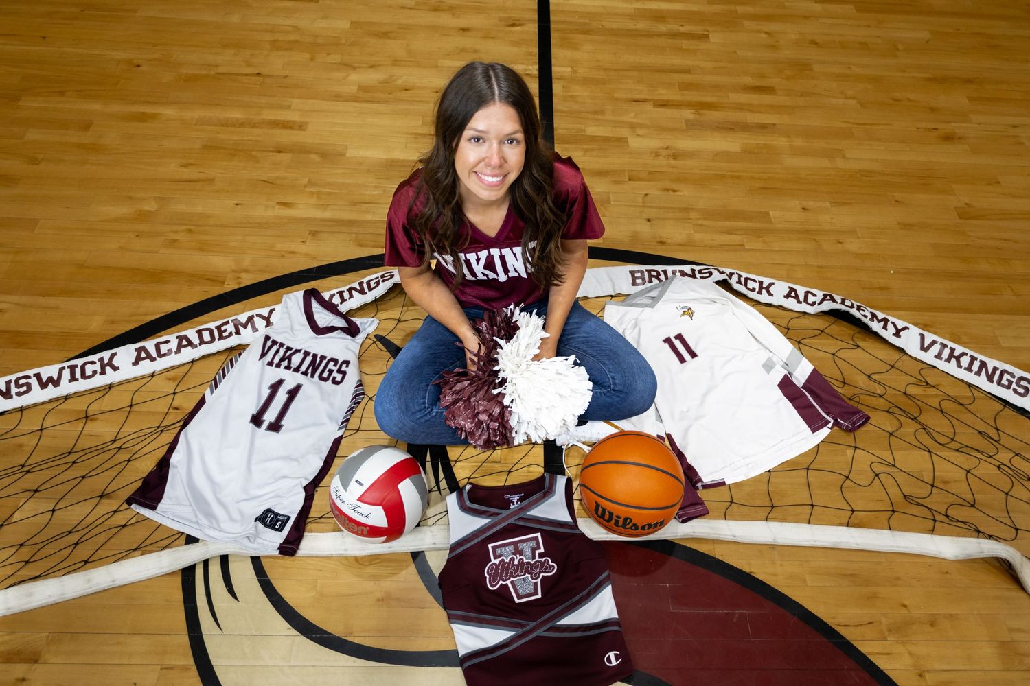 Basketball player in white uniform poses with ball on wooden court floor.