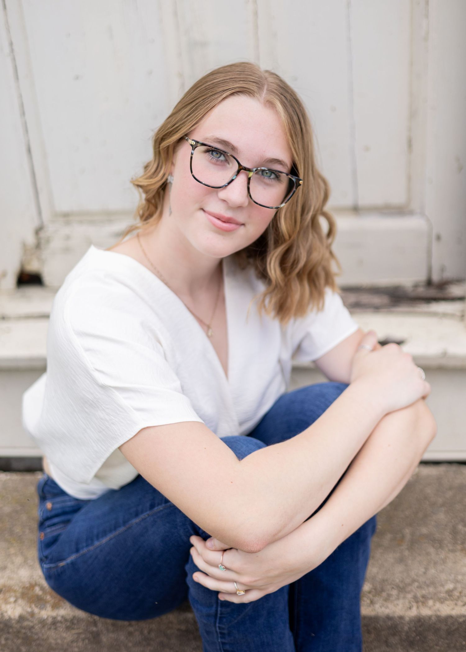 Casual senior portrait session against white wall wearing jeans and white top.