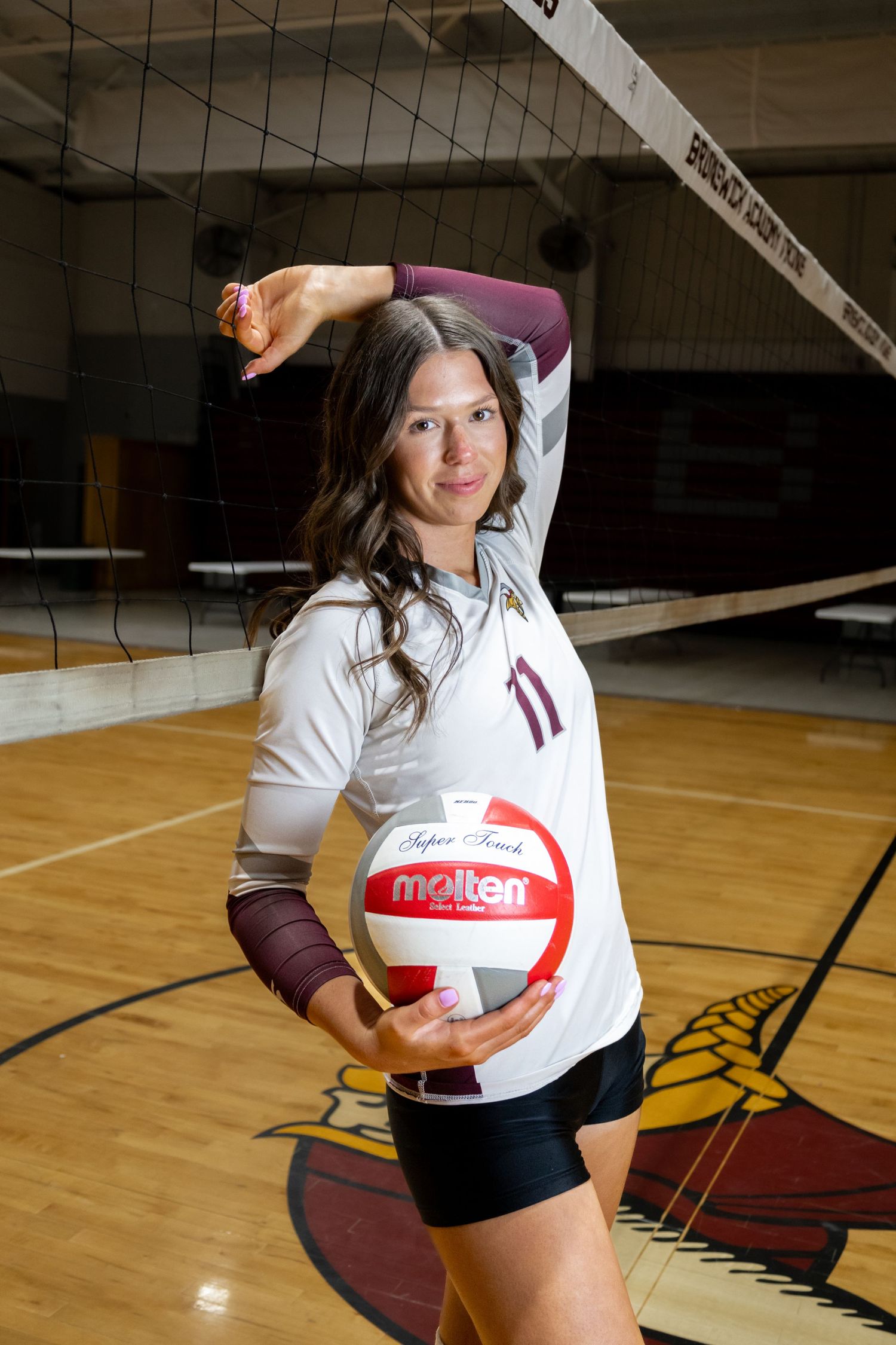 Volleyball player poses with ball in white uniform on indoor court.