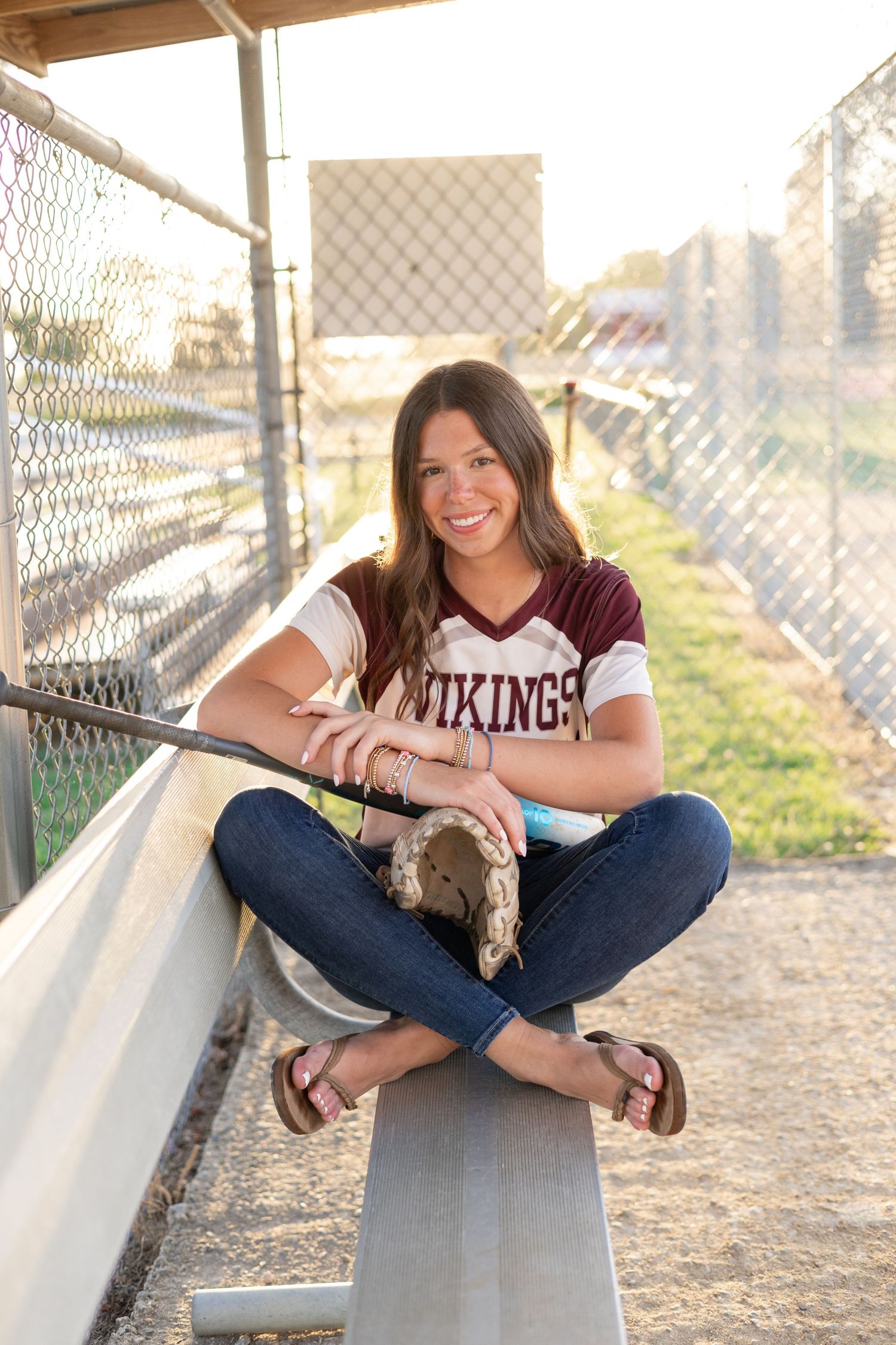 Senior portrait session at a baseball field with bleachers during golden hour.