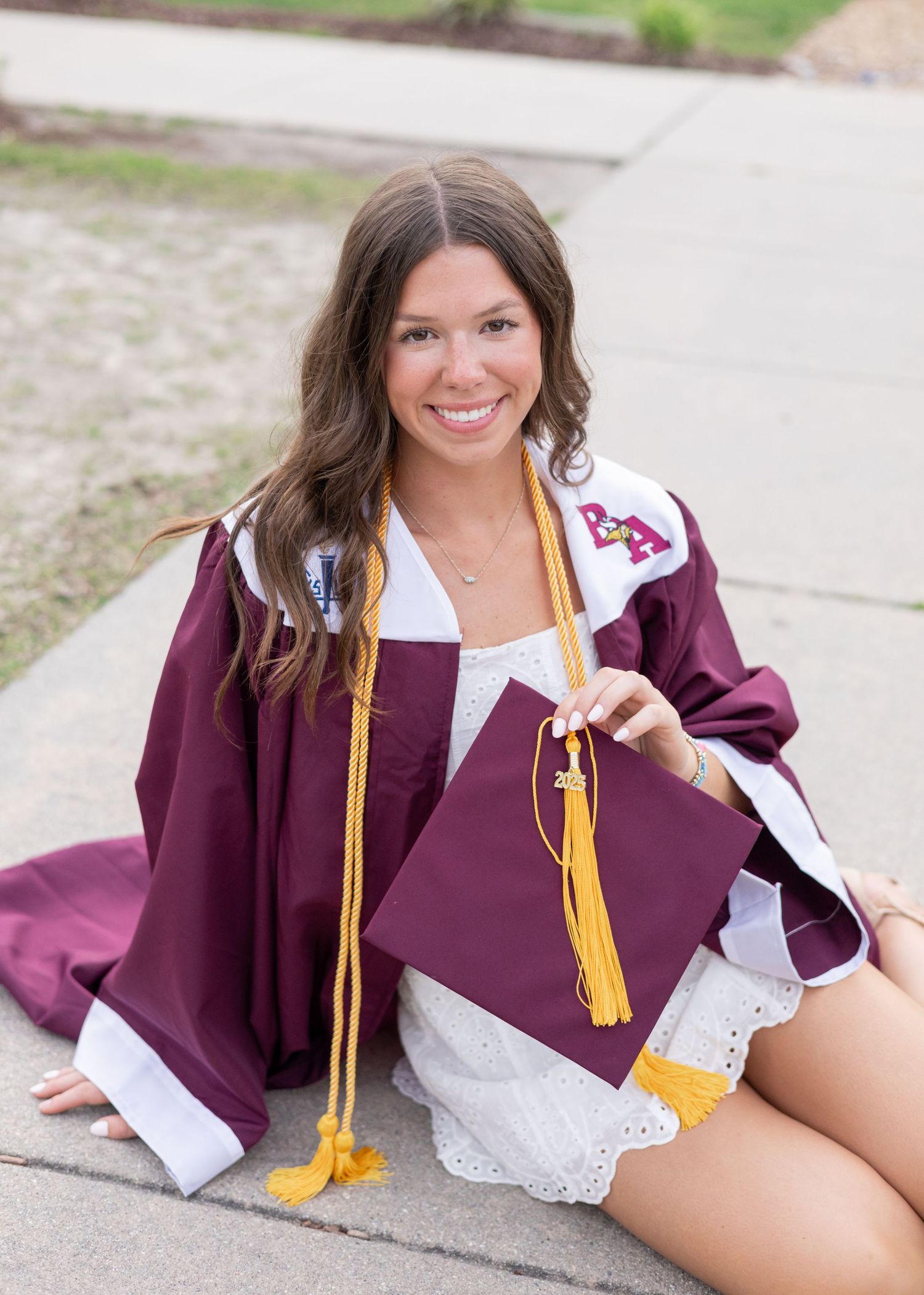 Graduate lying on ground in maroon graduation attire with gold tassel during photo session.