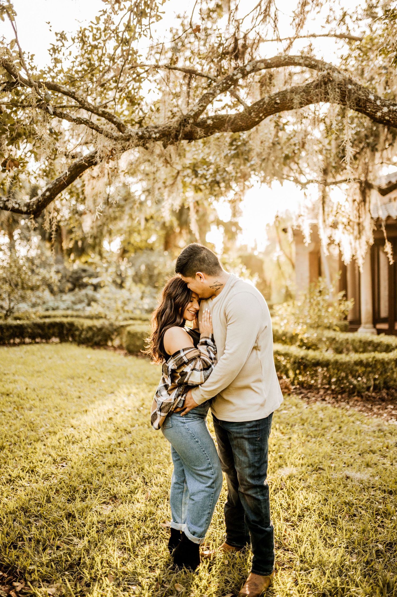 A romantic couple embracing under Spanish moss draped trees in golden light.