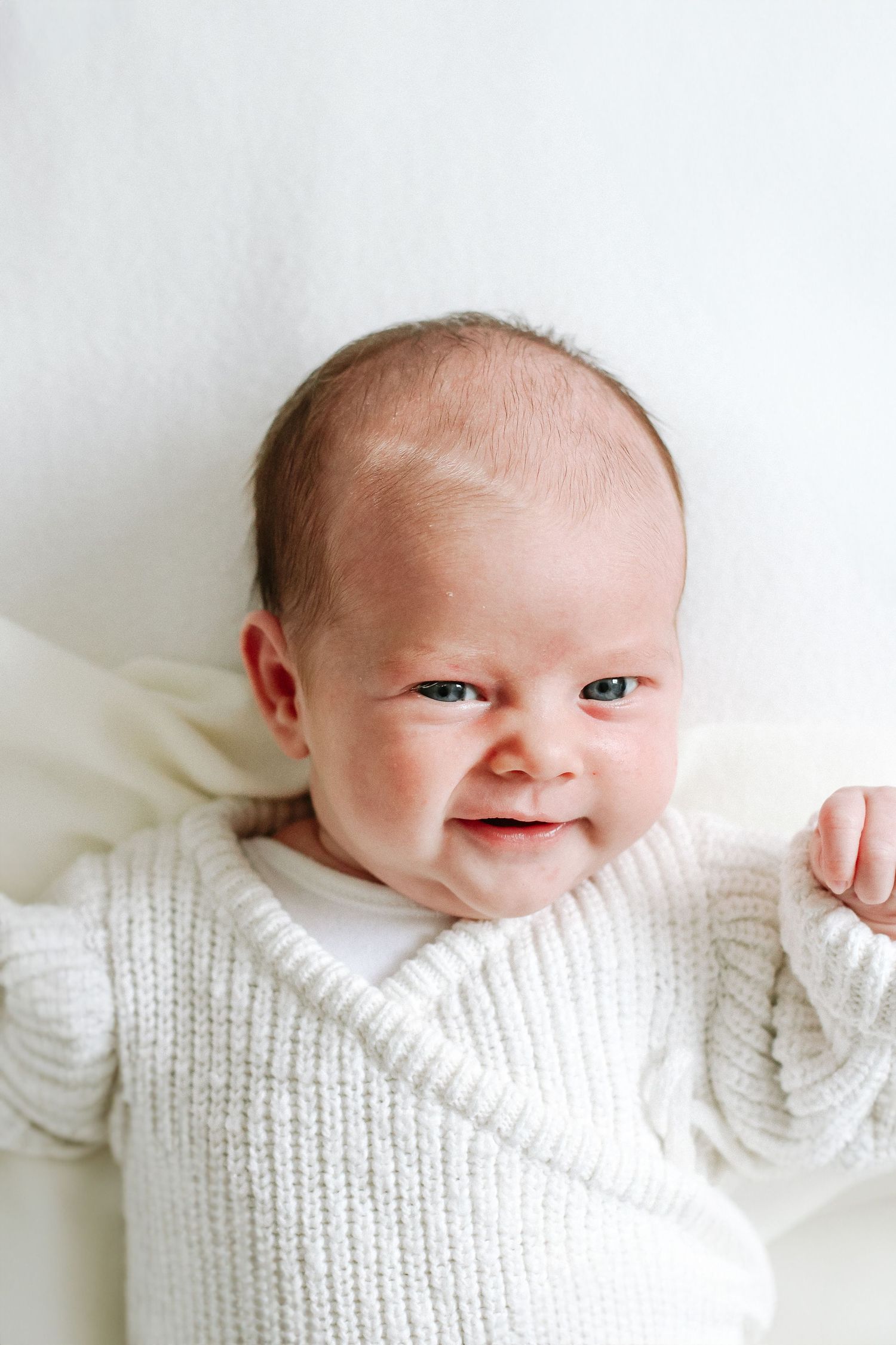 Photo showing a smiling baby wearing a cozy white knit romper against a light background, during newborn photoshoot in Nottingham