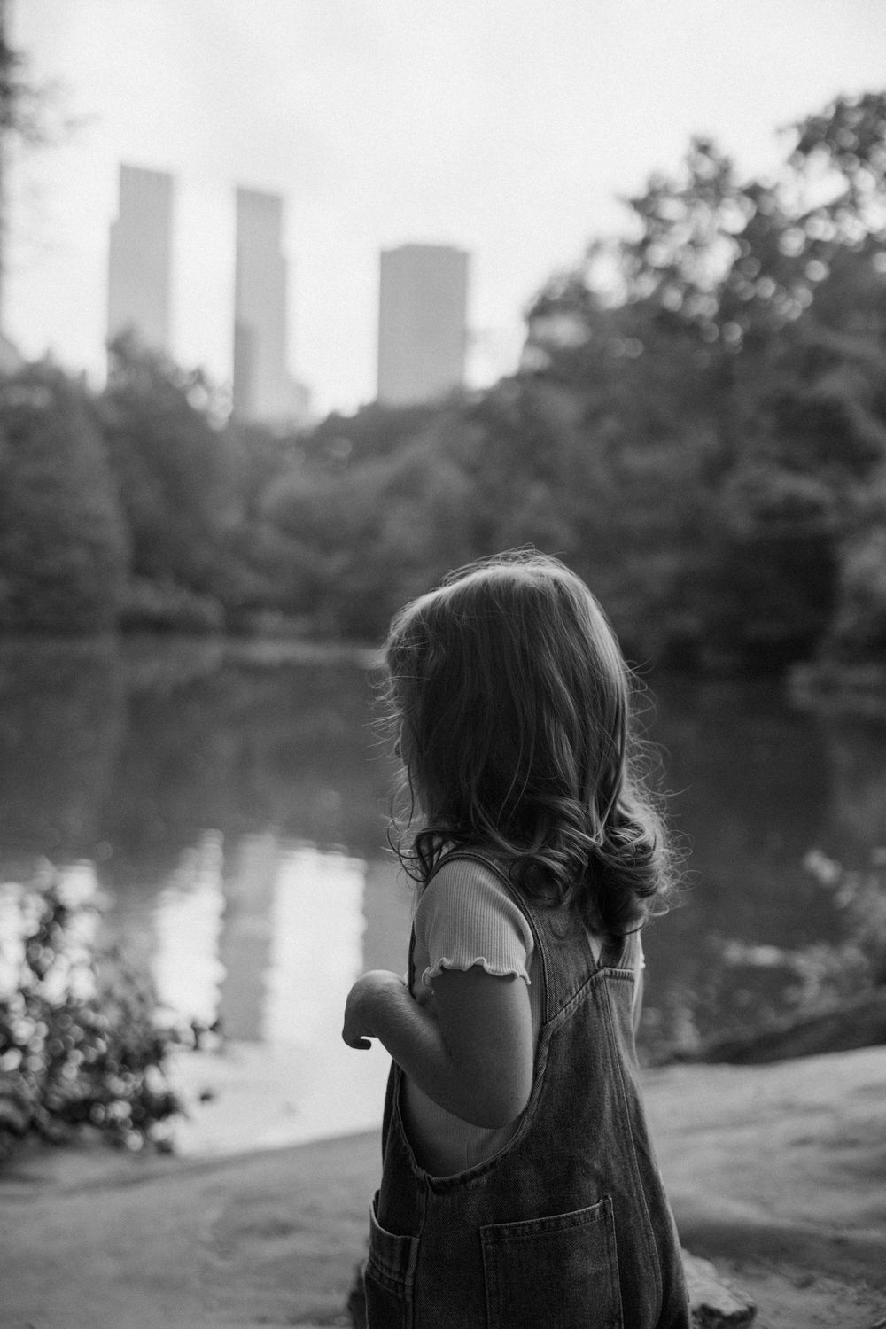 Artistic black and white photo series of a person viewed from behind near a lake with city buildings in the distance.