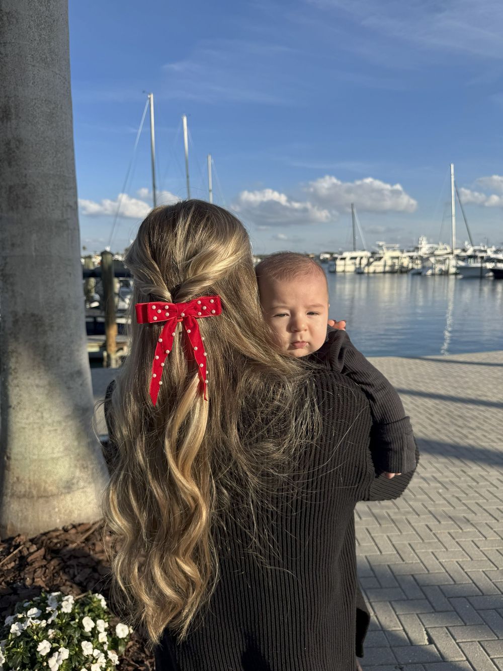 A scene at a marina with long wavy hair adorned with a red bow, against a backdrop of boats and blue sky.