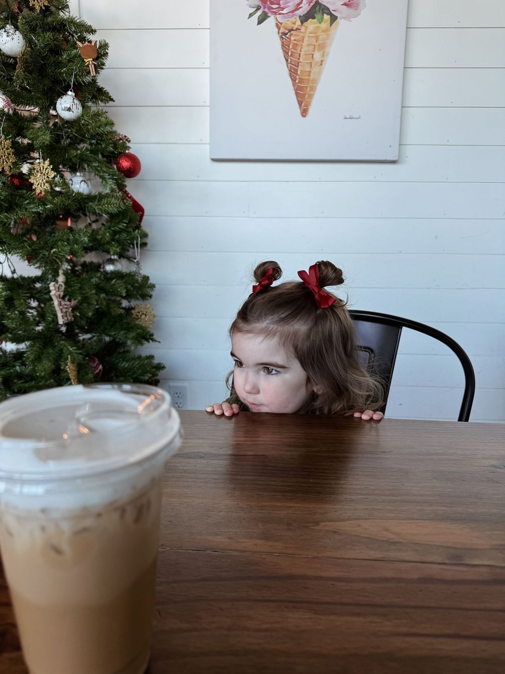 Four photos showing a coffee drink in a clear plastic cup sitting on a wooden table with a Christmas tree in the background.