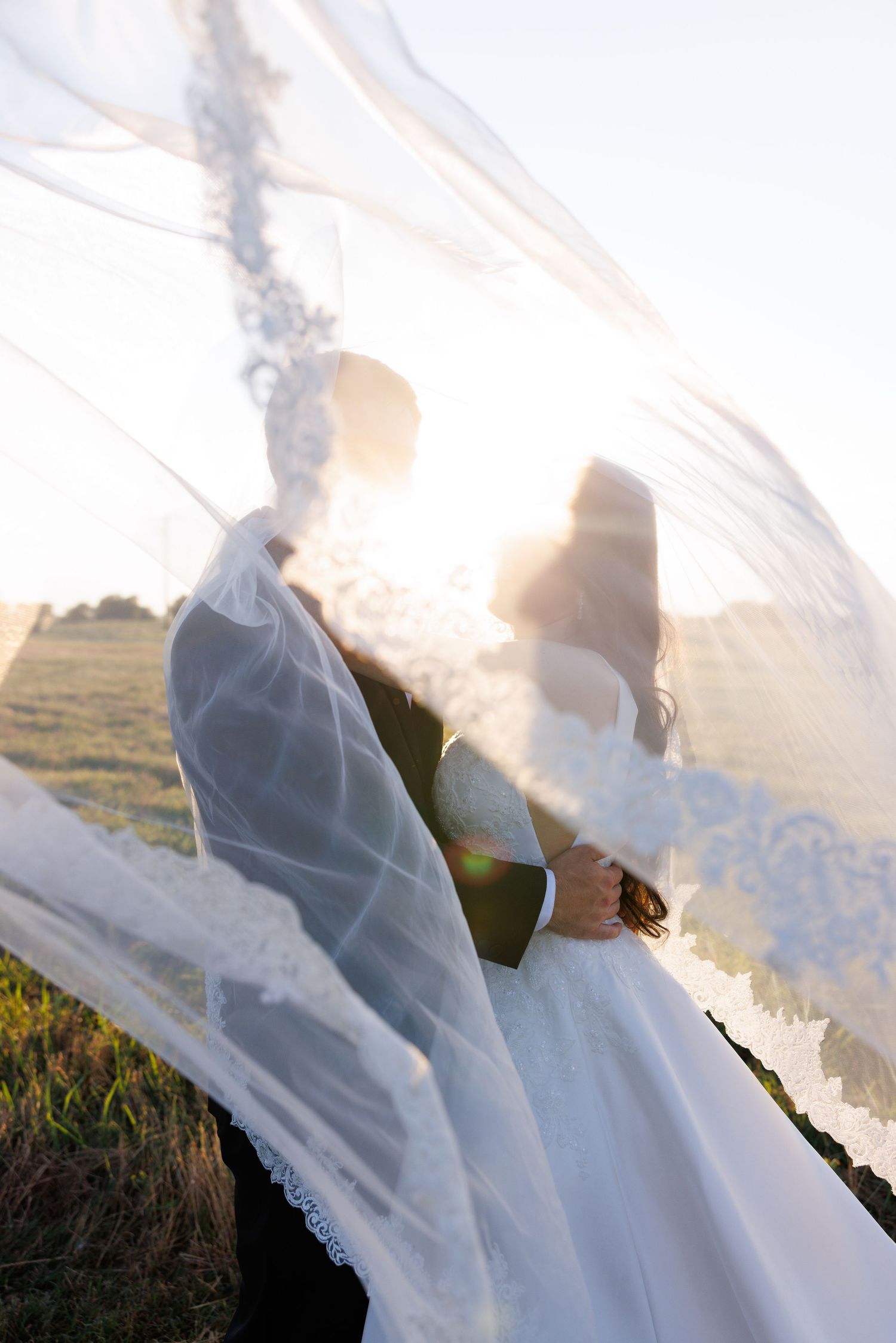 A flowing white wedding veil catches the wind against a bright sky.