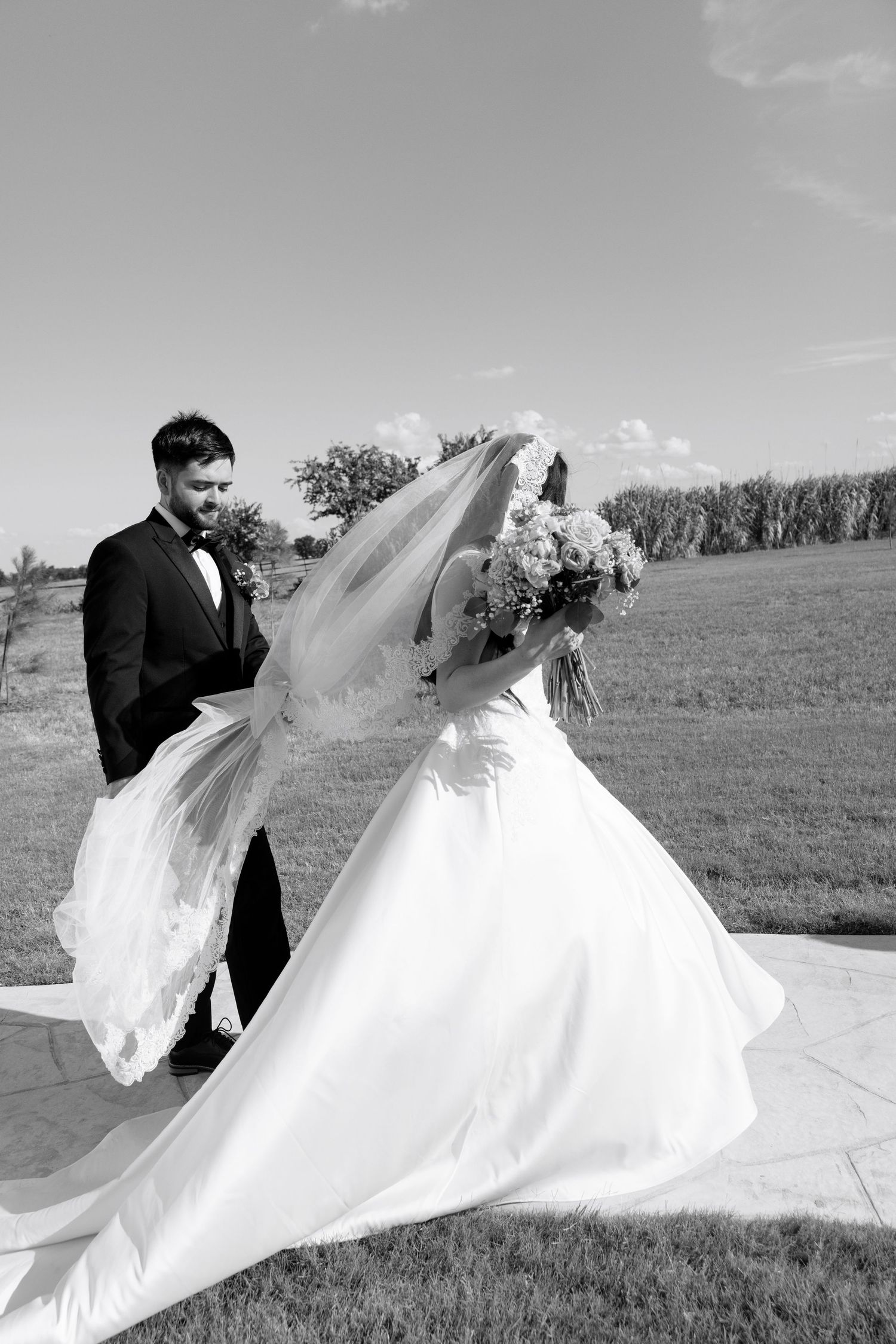 A flowing white wedding dress billows in the wind against a grassy field backdrop.