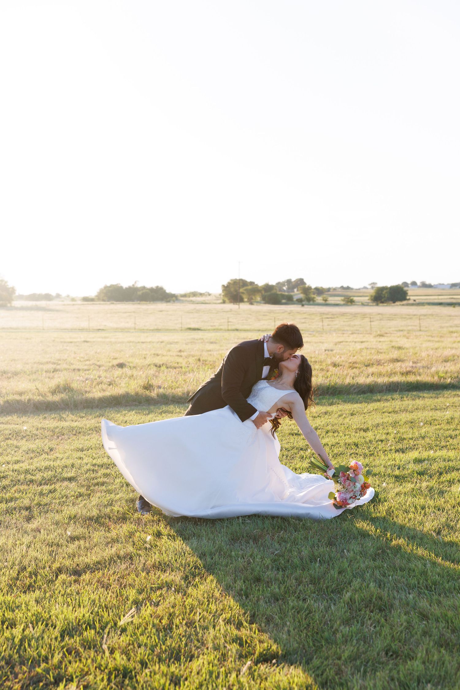 Newlyweds share a romantic moment while lying in a sunlit grassy field.