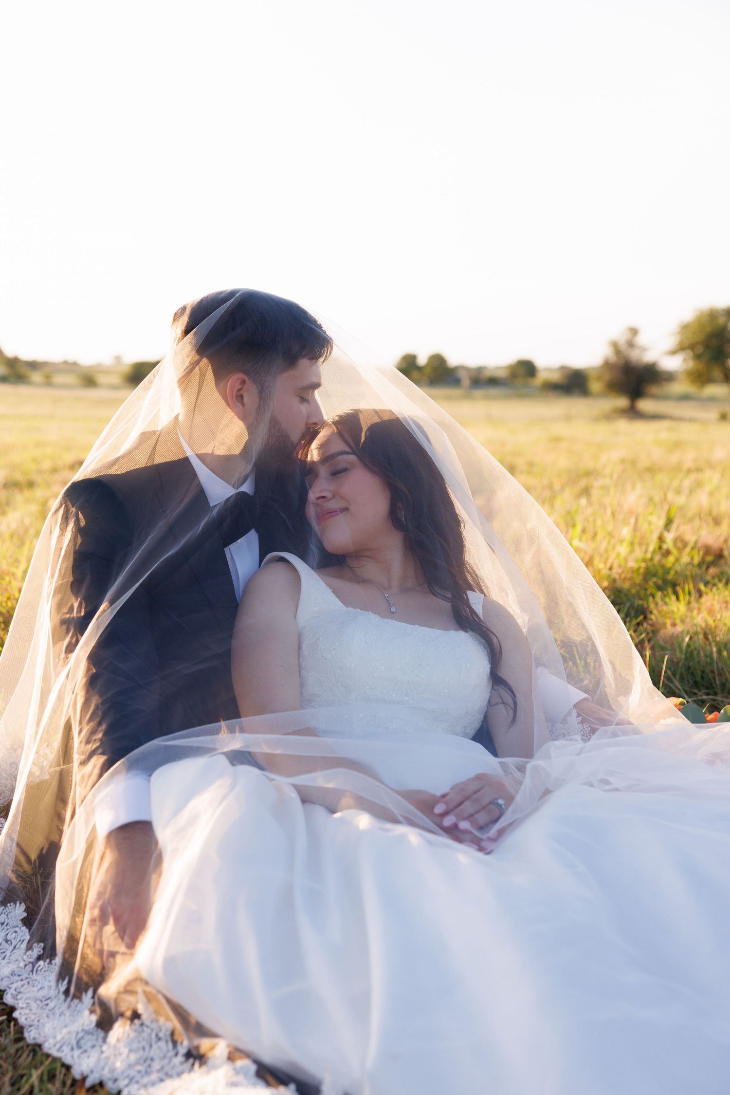 An intimate moment between newlyweds sitting in a golden field at sunset.