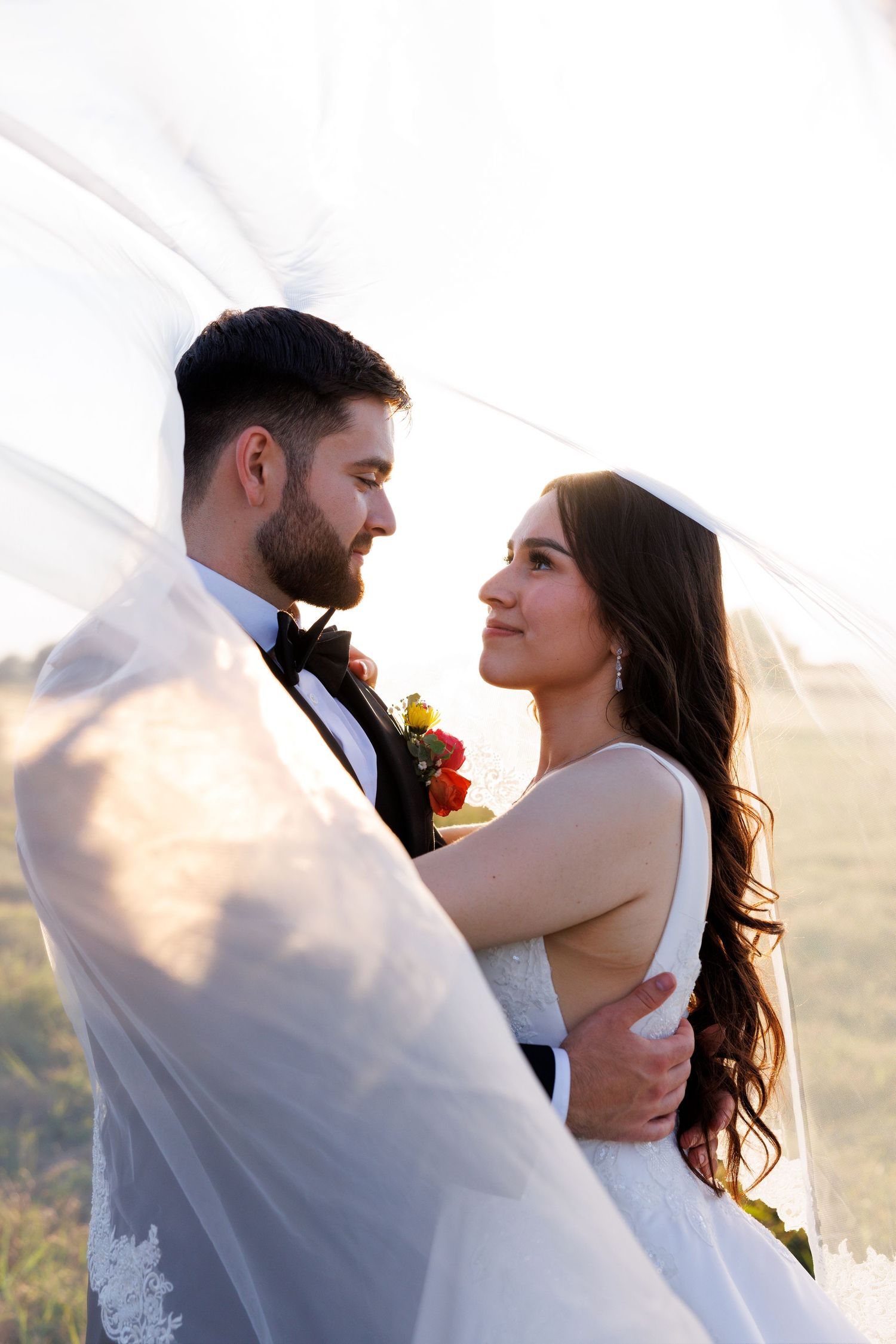 A tender embrace captured under flowing white veil during sunset.