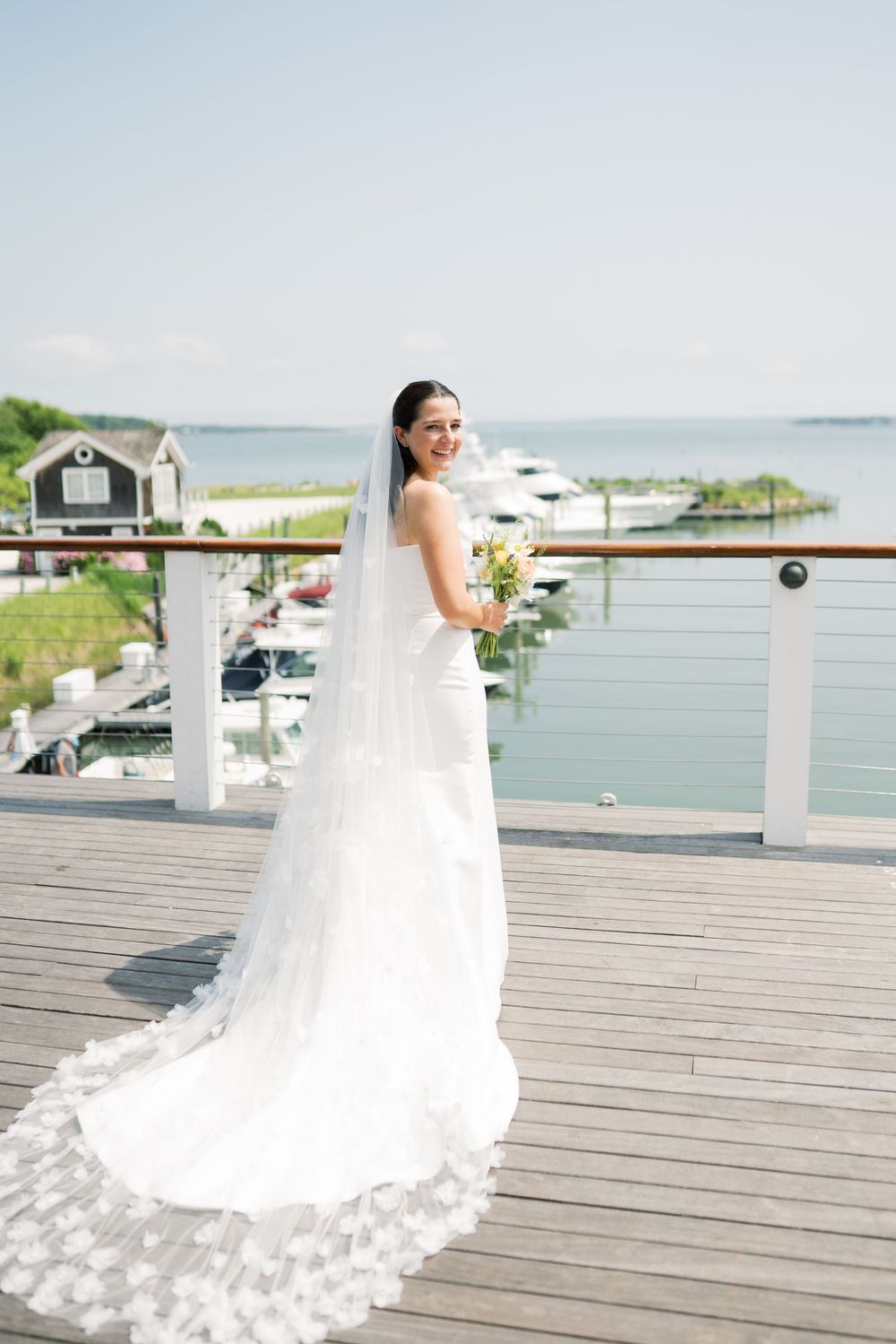 A bride in a stunning white gown poses on a marina deck with boats in the background.