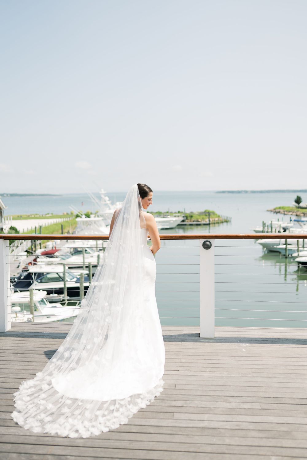 A flowing white wedding dress with a long train photographed on a waterfront wooden deck.