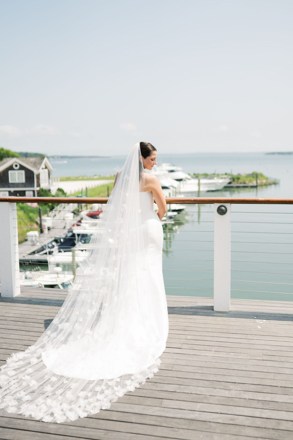 A flowing white wedding dress with long train photographed on a waterfront deck.