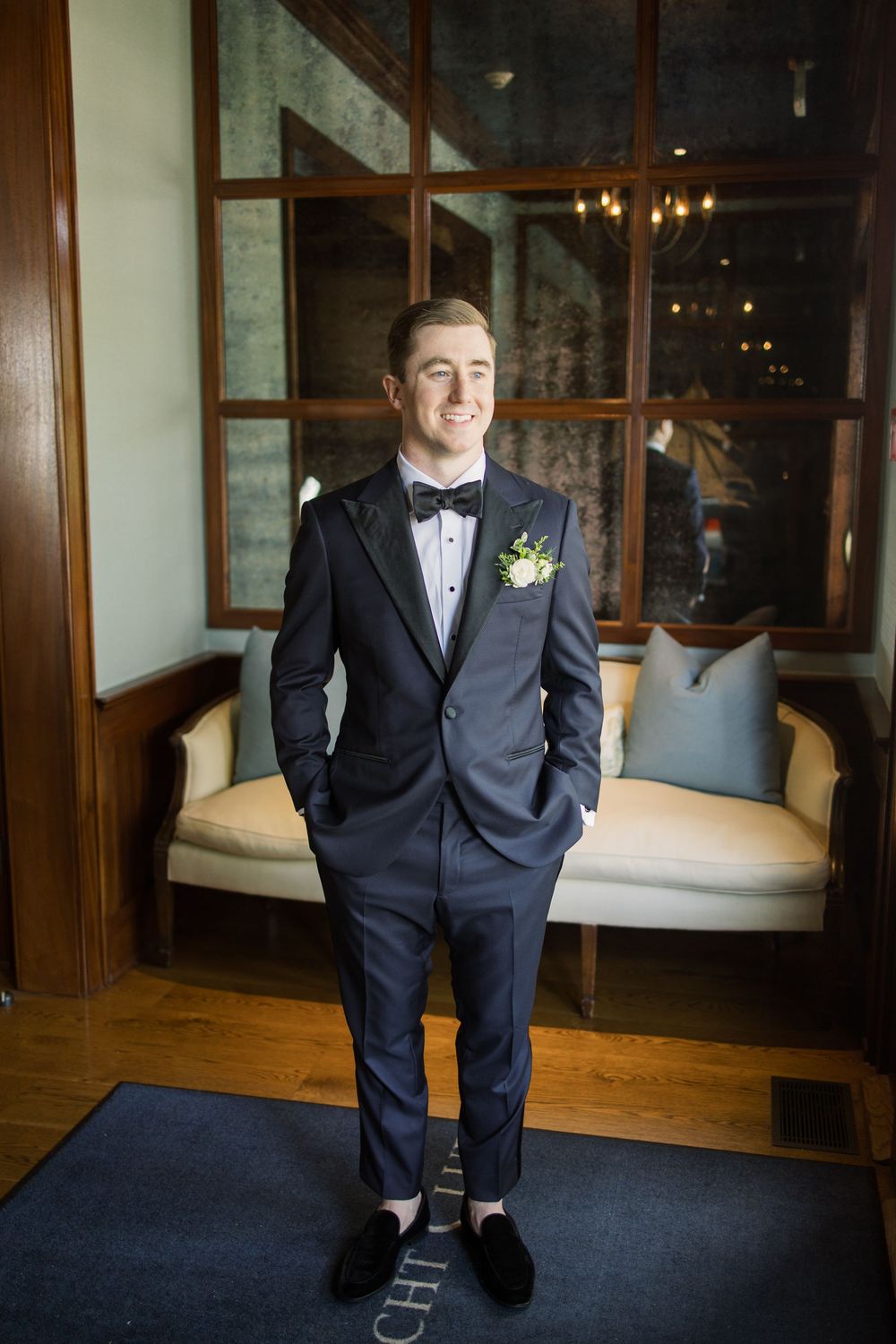 A groom in a classic navy tuxedo poses in an elegant indoor setting.