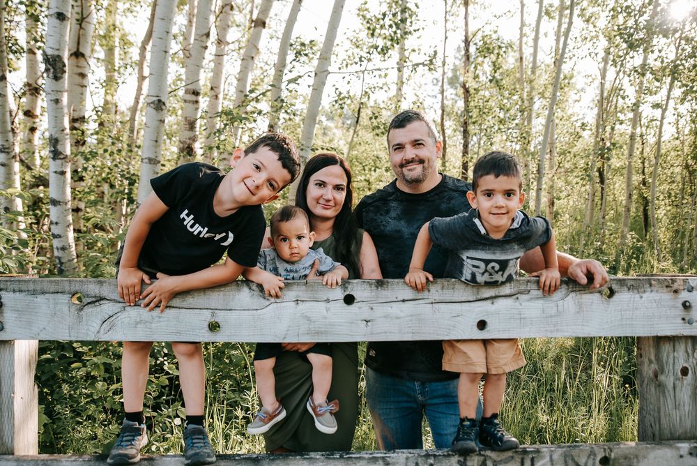 Family leaning on wooden railing with birch trees in background.