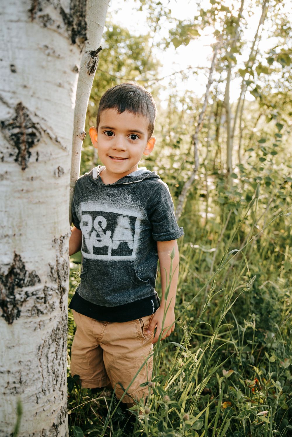 Young child standing next to white birch tree in natural setting.
