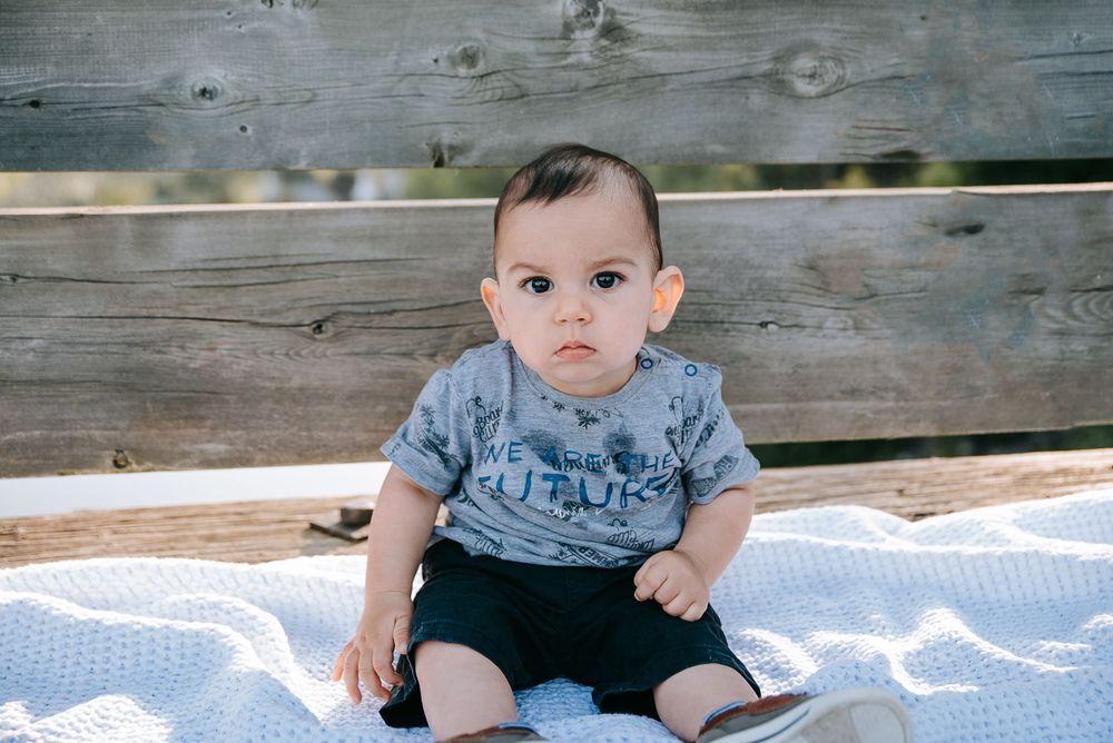 Baby sitting on blanket on wooden deck.