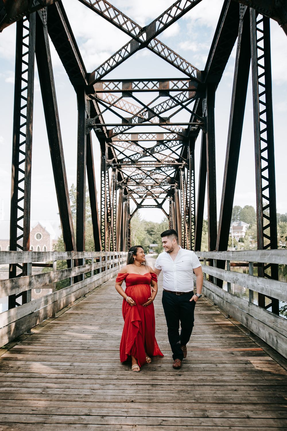 Couple walking on historic steel bridge with woman in flowing red dress.