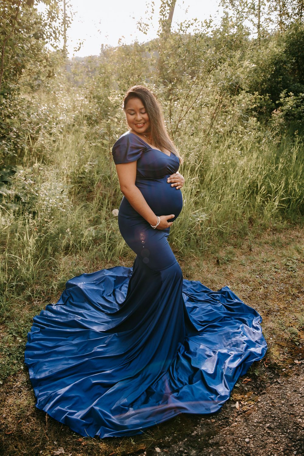 A dramatic maternity photo showing a flowing navy blue dress against a natural outdoor backdrop.