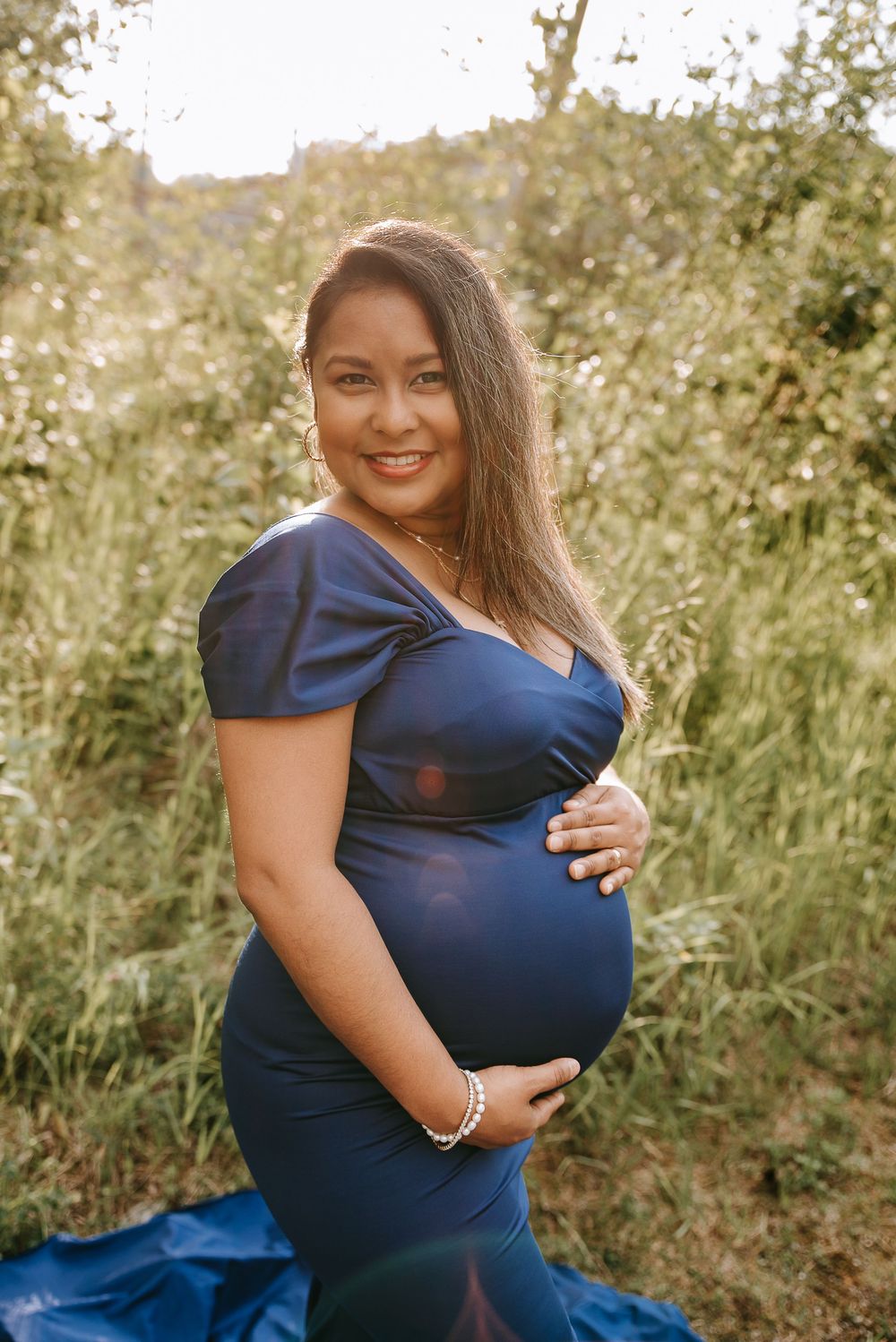 A maternity portrait outdoors featuring a woman in an elegant navy blue dress amid natural greenery.
