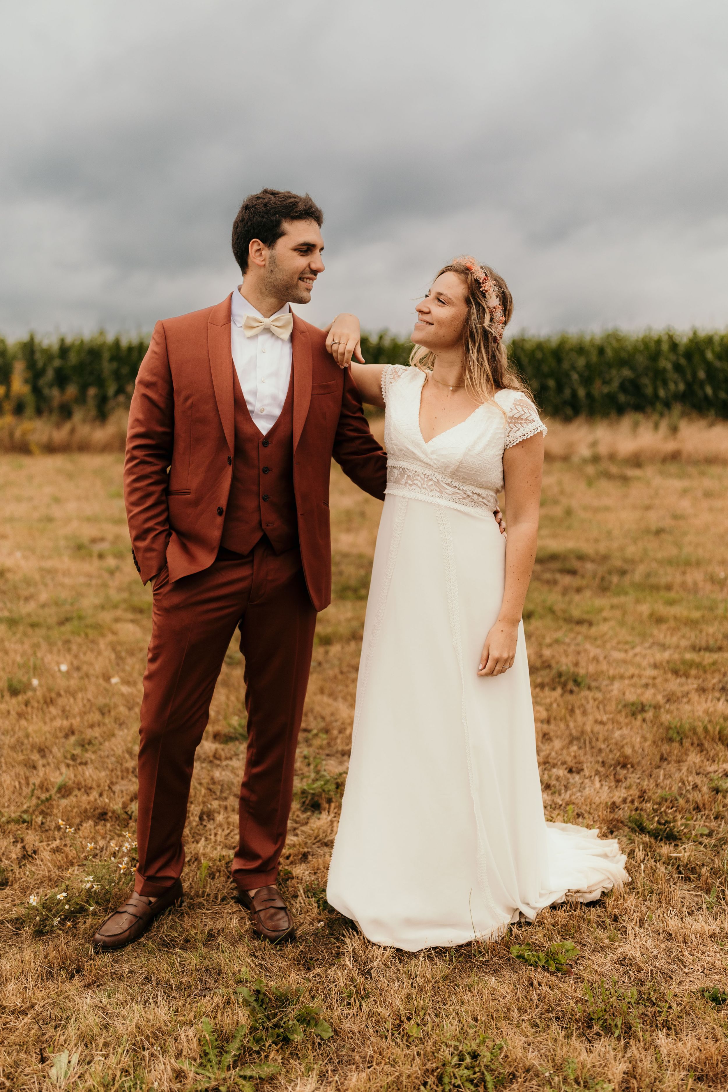 A couple in wedding attire shares a candid moment in a rustic field setting.