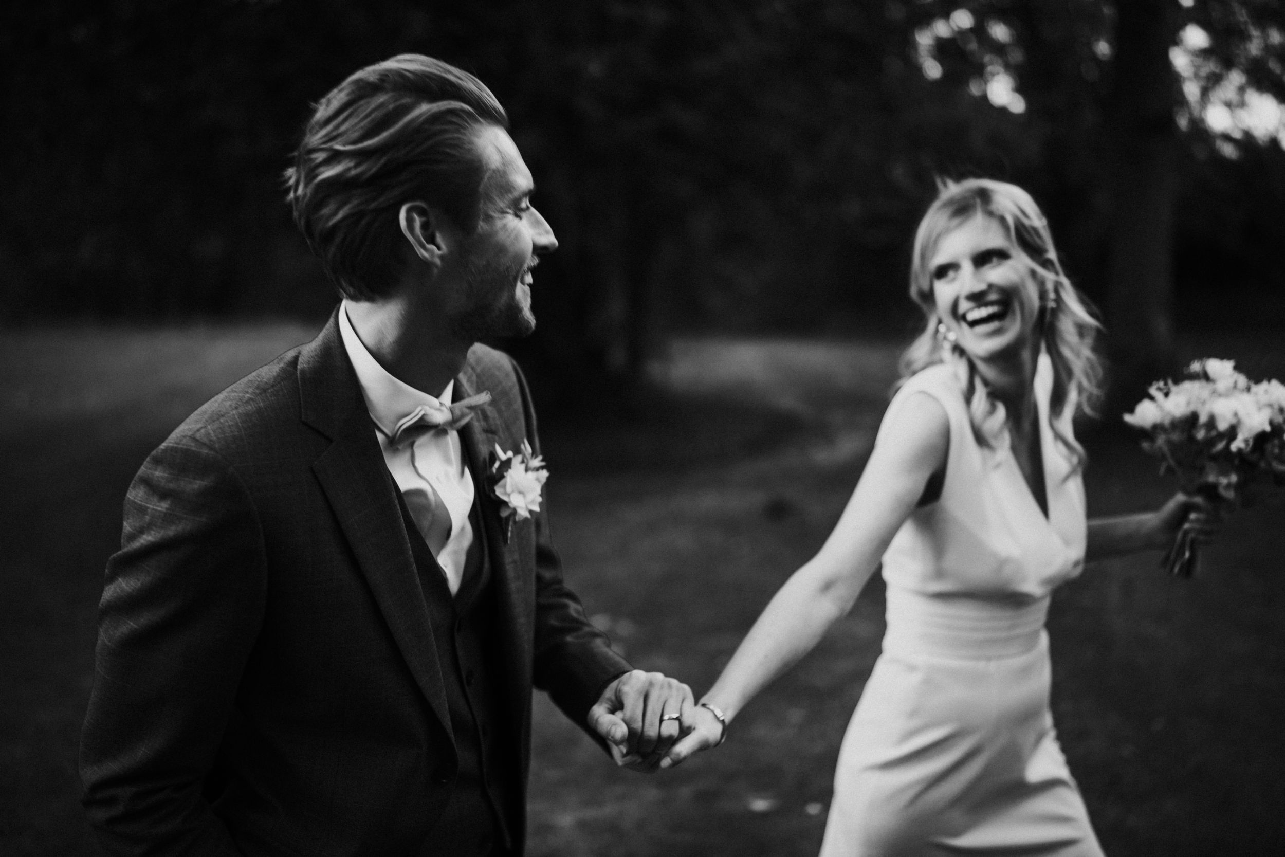 A black and white photo captures a playful moment between newlyweds in an outdoor setting.