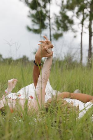 Person lying in tall grass wearing a white dress with floral details.