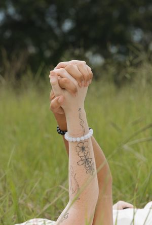 Close-up of tattooed arms with floral designs against green grass background.