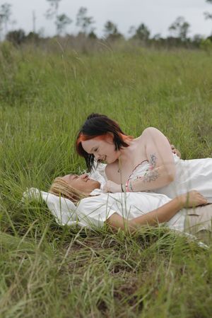 Person in white dress lying peacefully in tall grass during outdoor photo session.