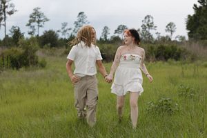 Couple walking hand in hand through a sunny meadow wearing coordinated outfits.