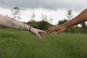 Close up of hands reaching towards each other against a blurred natural background.