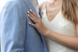Close-up of an engagement ring as bride touches groom's light blue suit jacket.