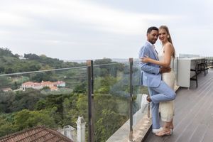 Couple shares tender moment on balcony overlooking tropical landscape.