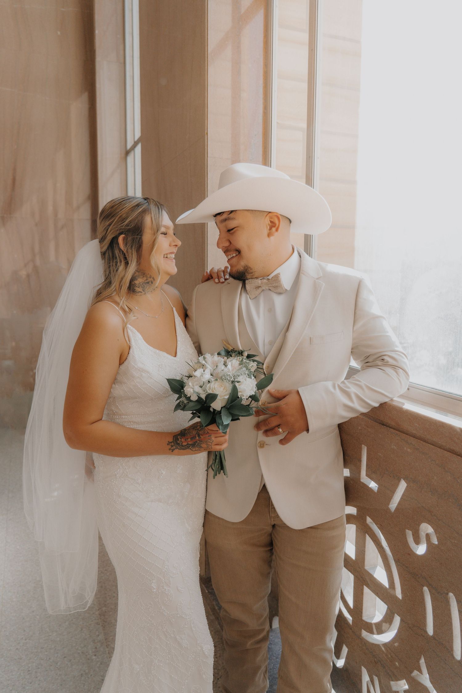 Rustic wedding couple in white and beige share intimate moment by window.