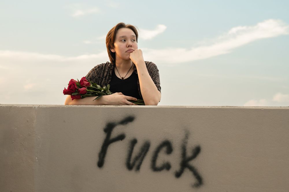 Dark graffiti text is spray painted on a concrete wall against a cloudy sky at dusk.