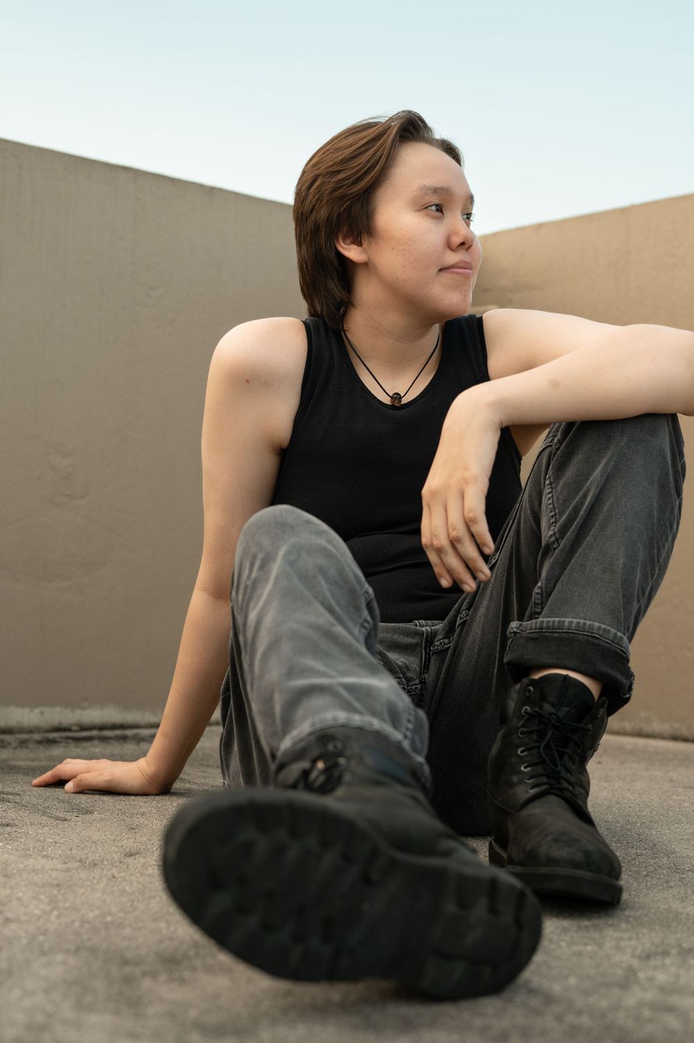 Someone in casual attire sits relaxed on a concrete surface wearing boots and a black tank top.